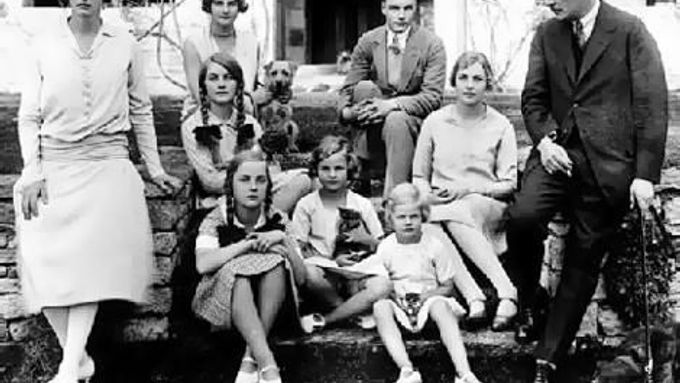 Rodinná fotka Mitfordů. Vlevo matka a v pravo otec, mezi nimi šest sester i jeden syn. Unity sedí jako první nalevo od otce