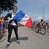 The pack of riders cycles past a French flag on Bastille day