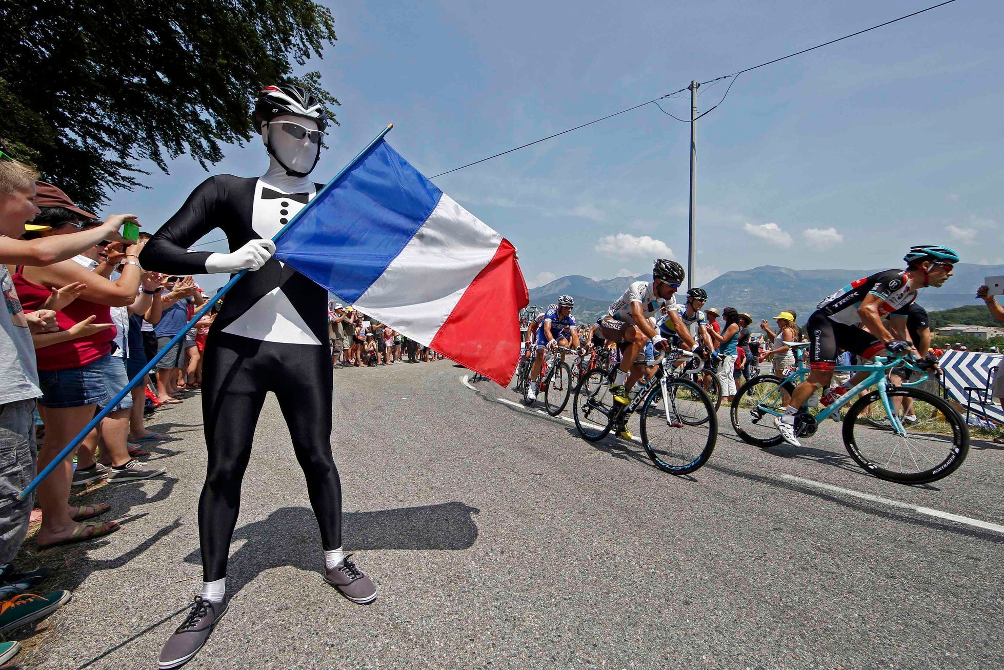 The pack of riders cycles past a French flag on Bastille day