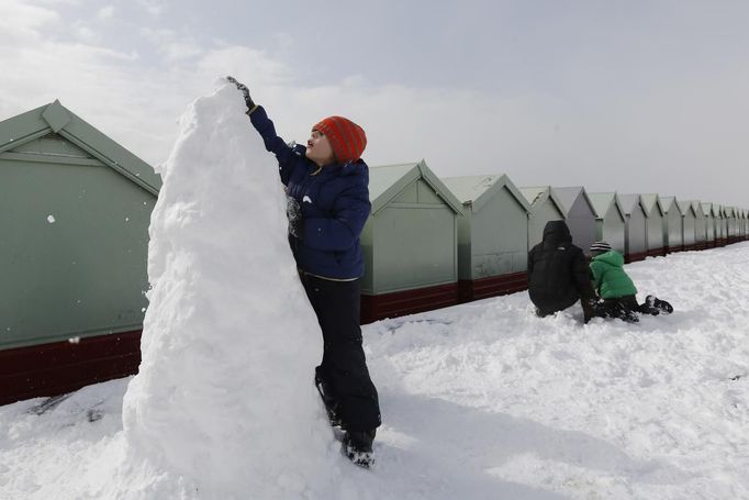 Joe Ottwell, age five, helps build a snowman with his family by beach huts in Brighton, southern England March 12, 2013. Southern England was hit with heavy snow overnight. REUTERS/Luke MacGregor (BRITAIN - Tags: ENVIRONMENT SOCIETY) Published: Bře. 12, 2013, 1:10 odp.