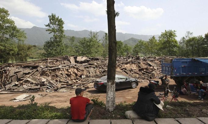 People sit near collapsed buildings after a strong 6.6 magnitude earthquake, at Longmen village, Lushan county, Ya'an, Sichuan province, April 20, 2013. The earthquake hit a remote, mostly rural and mountainous area of southwestern China's Sichuan province on Saturday, killing at least 102 people and injuring about 2,200 close to where a big quake killed almost 70,000 people in 2008. REUTERS/Stringer (CHINA - Tags: DISASTER) CHINA OUT. NO COMMERCIAL OR EDITORIAL SALES IN CHINA Published: Dub. 20, 2013, 9:22 dop.