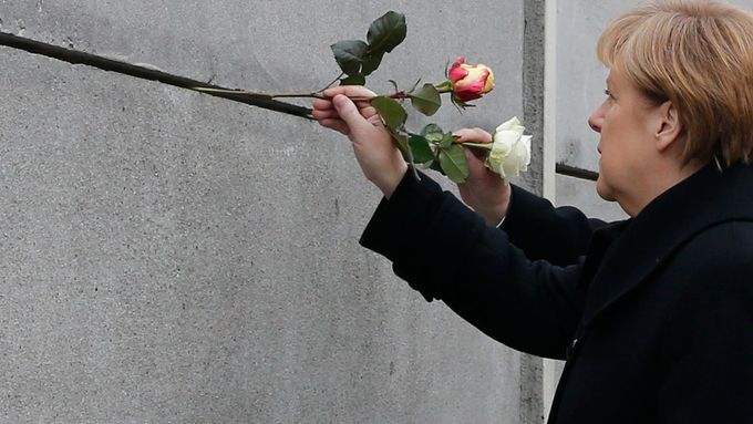 Německá kancléřka Angela Merkelová zasouvá květinu do Berlínské zdi.  Snímek z oslav 25. výročí pádu tohoto symbolu rozděleného Německa.