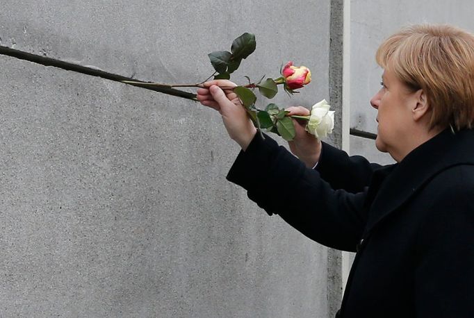 Německá kancléřka Angela Merkelová zasouvá květinu do Berlínské zdi.  Snímek z oslav 25. výročí pádu tohoto symbolu rozděleného Německa.