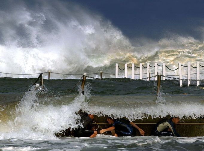 Chlapci se krčí za příbojovou bariérou během jejich hry v silném vlnobití na pláži Narrabeen Beach v Sydney, 26. února 2004. Obrovské vlny udeřily na pláže v Sydney během noci jakožto výsledek kombinace silného větru a nízkého tlaku na východním pobřeží Austrálie. REUTERS/David Gray