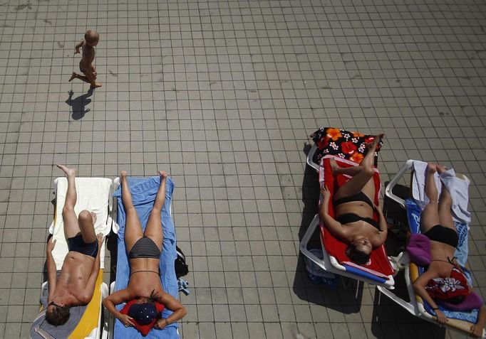 People sunbath as a child runs past them at the public swimming pool Kongressbad in Vienna June 30, 2012. Temperatures will rise up to 37 degrees Celsius (98.6 Fahrenheit) in Austria in the next days, Austria's national weather service agency ZAMG reported. REUTERS/Lisi Niesner (AUSTRIA - Tags: ENVIRONMENT TPX IMAGES OF THE DAY) Published: Čer. 30, 2012, 2:24 odp.