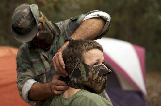 A member of the North Florida Survival Group puts a mask on his son as they gear up to perform enemy contact drills in a wooded area during a field training exercise in Old Town, Florida, December 8, 2012. The group trains children and adults alike to handle weapons and survive in the wild. The group passionately supports the right of U.S. citizens to bear arms and its website states that it aims to teach "patriots to survive in order to protect and defend our Constitution against all enemy threats". Picture taken December 8, 2013. REUTERS/Brian Blanco (UNITED STATES - Tags: SOCIETY POLITICS) ATTENTION EDITORS: PICTURE 4 OF 20 FOR PACKAGE 'TRAINING CHILD SURVIVALISTS' SEARCH 'FLORIDA SURVIVAL' FOR ALL IMAGES Published: Úno. 22, 2013, 1 odp.