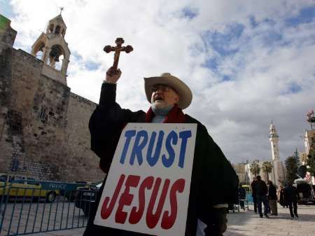 Důvěřuj Ježíšovi, hlásá transparent, který před chrámem v Betlémě nese křesťanský poutník