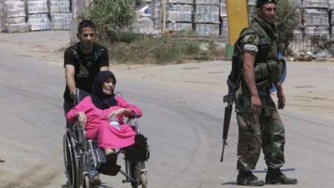 Žena na invalidním vozíčku opouští kvůli bojům tábor Nahr Bárid.