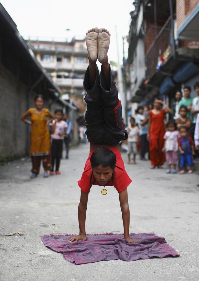 People watch as Drumpal Choudhary, 11, a street performer, performs his tricks on a street in Kathmandu August 15, 2012. Drumpal and his siblings Shivani and Gchan, who came to Kathmandu from India 5 years ago, earn their living by performing tricks on the streets of Kathmandu. According to Drumpal they earn around $10 a day by performing tricks, which is not enough to feed their 10-member family living together in a small hut without a proper toilet or any basic needs. REUTERS/Navesh Chitrakar (NEPAL - Tags: SOCIETY POVERTY IMMIGRATION) Published: Srp. 15, 2012, 4:36 odp.