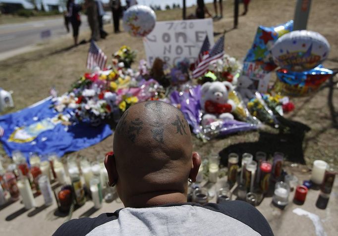 A man sits in front of a memorial site for victims behind the theater where a gunman opened fire on moviegoers in Aurora, Colorado July 21, 2012. Colorado authorities are preparing a series of "controlled detonations" in the booby-trapped apartment of James Holmes who is accused of going on a shooting rampage in a crowded movie theatre, which killed 12 people and wounded dozens more, during a showing of the new "Batman" film, police said on Saturday. REUTERS/Shannon Stapleton (UNITED STATES - Tags: ENTERTAINMENT CRIME LAW DISASTER SOCIETY) Published: Čec. 21, 2012, 6:42 odp.