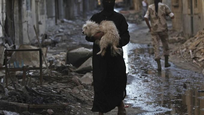 Muž nese psa přes zablácenou ulici v Sýrii. Ilustrační foto.