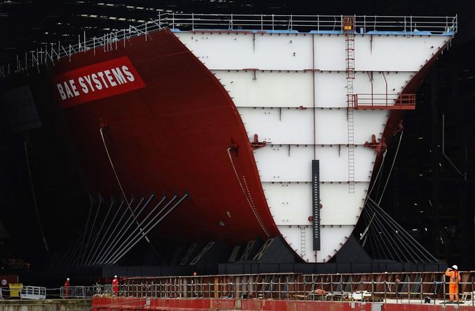 Workers watch as the forward section of the aircraft carrier HMS Queen Elizabeth is moved onto a barge at HM Naval Base in Portsmouth, southern England May 14, 2012. The hull will be transported by a sea going barge to Rosyth in Scotland where the ship will be assembled in dry dock. REUTERS/Luke MacGregor (BRITAIN - Tags: BUSINESS EMPLOYMENT MILITARY) Published: Kvě. 14, 2012, 2:27 odp.