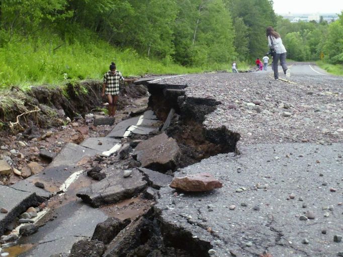 A woman stands in a sunken street after flooding in Duluth, Minnesota, June 20, 2012. Heavy rains pounded northern Minnesota on Wednesday, forcing the evacuation of dozens of homes, causing mudslides and sinkholes, and swamping a zoo where several animals died, officials said. Picture taken June 20, 2012. REUTERS/Joe Cadotte (UNITED STATES - Tags: DISASTER SOCIETY ENVIRONMENT) Published: Čer. 21, 2012, 10:48 odp.