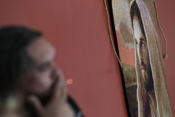 Catholic priest Adolfo Huerta, known as "Gofo", smokes a cigarette while standing next to a painting of Jesus Christ in Saltillo February 22, 2013. Ordained five years ago, Huerta is an unconventional priest who likes rock music, dyes the ends of his hair red, dresses in black, and enjoys riding his motorcycle. Huerta found God and priesthood while studying philosophy at the Pontifical University in Mexico City and working with HIV-positive patients and sex workers as a social activist. He says it is important to demystify faith and accept people's differences without judgment, and in his sermons he references rock songs, quotes books and tells jokes. Picture taken February 22, 2013. REUTERS/Daniel Becerril (MEXICO - Tags: RELIGION SOCIETY) ATTENTION EDITORS: PICTURE 26 OF 26 FOR PACKAGE 'CHURCH, FAITH AND ROCK'N ROLL' SEARCH 'PRIEST DANIEL' FOR ALL IMAGES Published: Bře. 15, 2013, 10:24 dop.