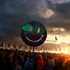 A smiley face is held up by a festival-goer as the sun sets in front of the Other Stage at Worthy Farm in Somerset, during the Glastonbury Festival