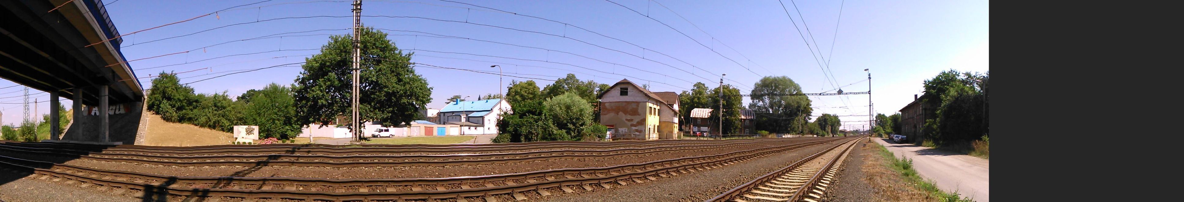 Panorama: pomník s mostem na jedné straně, napravo tam, kde se stýkají koleje, je nádraží, kde stojí trosky Pendolina.