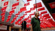 Muž prochází kolem rozsvíceného obchodního centra v Hongkongu, kde vlajky zdobí celé fasády, město se tak přidává k celonárodním oslavám.
