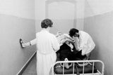 Dobový text: "Večer na záchytné stanici U Apolináře v Praze, 1. června 1973. Někdy je zachycený nebezpečný sobě i svému okolí natolik, že musí být na záchytné stanici izolován v místnosti a připoután na lůžko. Když se podaří personálu záchytné stanice pacienta spoutat, sestra mu dá pro uklidnění injekci."