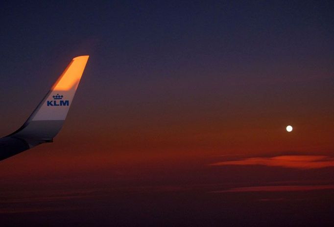 Zapadající slunce pableskuje na křídle letounu aerolinek KLM, který se vznáší nad Athénami. Na oblohu už vystoupal i měsíc v úplňku.