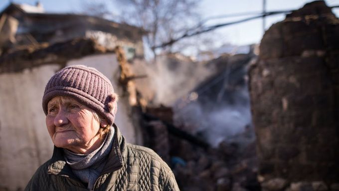 Stará žena před vybombardovaným domem ve východoukrajinské Avdějevce.
