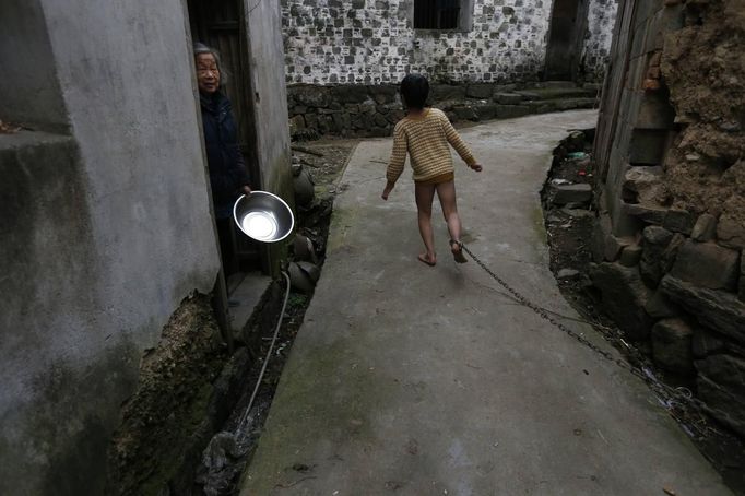 A boy runs past a neighbour along an alley outside his home as his father pulls on the chain locked around his ankle, in Zhejiang province