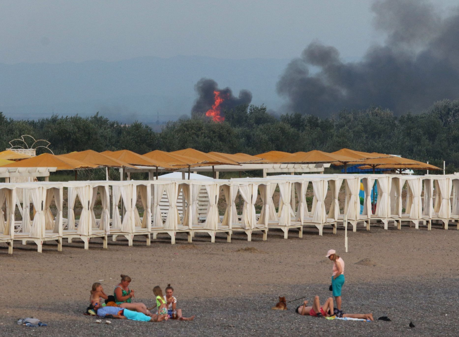 Skupina Rusů je na krymské pláži, zatímco v pozadí hoří letecká základna Saky.