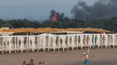 Skupina Rusů je na krymské pláži, zatímco v pozadí hoří letecká základna Saky.