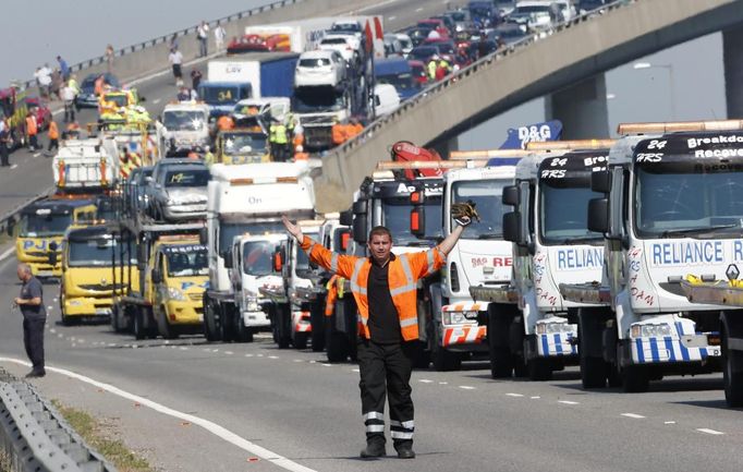 A rescue worker gestures in front of recovery trucks lined up to collect over 100 vehicles involved in multiple collisions, which took place in dense fog during the morning rush hour, on the Sheppey Bridge in Kent, east of London, September 5, 2013. Eight people were seriously injured and dozens hurt in the multiple crashes.