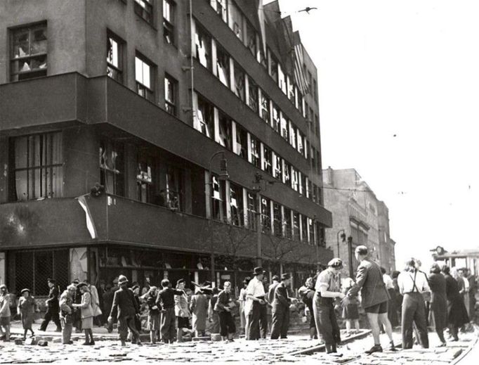 Ćeští občané přivolaní rozhlasem staví barikády před jeho budovou na Vinohradské třídě. Pražské povstání 1945 je v plném proudu.