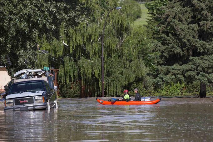 Dva muži odplouvají na loďce poté, co zkontrolovali svůj zaplavený dům v Calgary