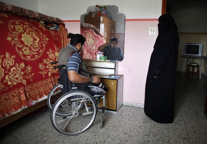 Wheelchair-bound Palestinian freelance photographer Moamen Qreiqea combs his hair as his mother watches in his home in Gaza City October 1, 2012. Qreiqea, 25, lost both his legs in an Israeli air strike in 2008 while taking pictures east of Gaza. The father of two is determined to continue his career despite his disability. REUTERS/Suhaib Salem (GAZA - Tags: MEDIA SOCIETY) Published: Říj. 1, 2012, 3:39 odp.