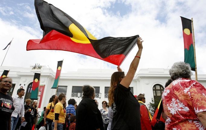 Demonstranti mávají australskou aboriginskou vlajkou.