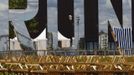 Picnic tables are stored next to a large mirrored word "RUN" in the London 2012 Olympic Park at Stratford in London July 12, 2012. Preparations for the London Olympics have put Britain's intelligence agencies under significant pressure, as the country stages its largest ever peacetime security operation, MPs said on Thursday. REUTERS/Luke MacGregor (BRITAIN - Tags: SPORT OLYMPICS) Published: Čec. 12, 2012, 6:29 odp.