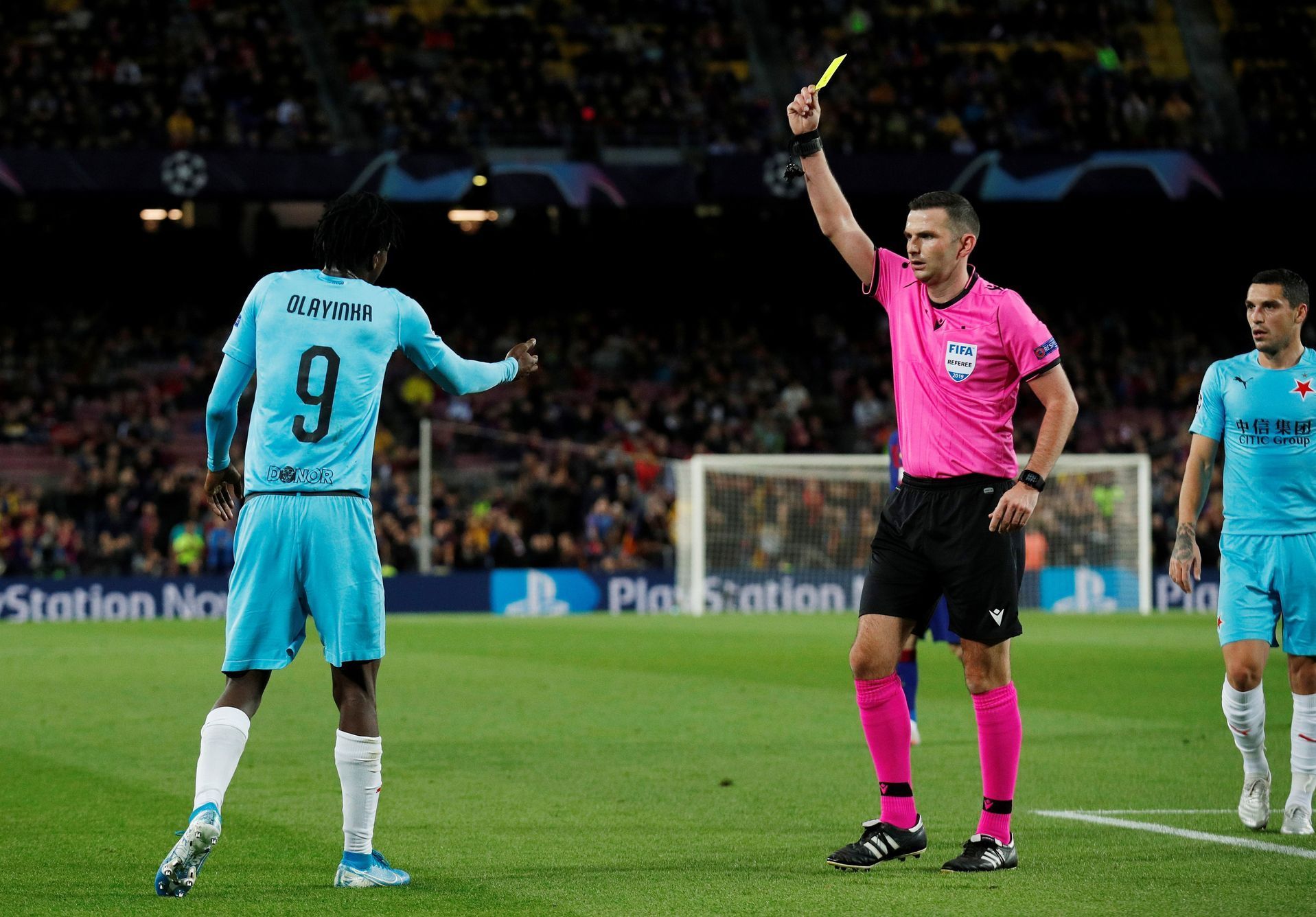 Peter Olayinka dostává žlutou kartu od rozhodčího Michaela Olivera v zápase LM Barcelona - Slavia Praha