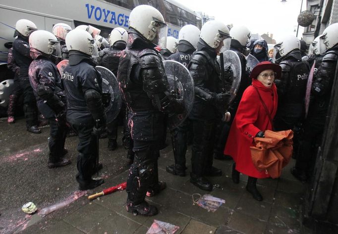 A woman walks behind Belgian riot policemen during clashes with Arcelor Mittal workers from several Liege steel plants demonstrating outside the Walloon Region parliament in Namur January 29, 2013. Arcelor Mittal, the world's largest steel producer, plans to shut a coke plant and six finishing lines at its site in Liege, Belgium, affecting 1,300 employees, the group said last week. REUTERS/Yves Herman (BELGIUM - Tags: CIVIL UNREST BUSINESS EMPLOYMENT COMMODITIES) Published: Led. 29, 2013, 1:22 odp.