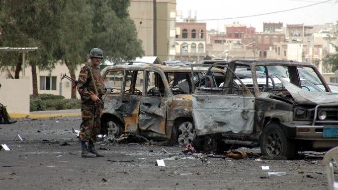 Den poté. Jemenský voják postává před dvojicí vyhořelých vraků vozů v blízkosti americké ambasády v hlavním městě Sana'á.