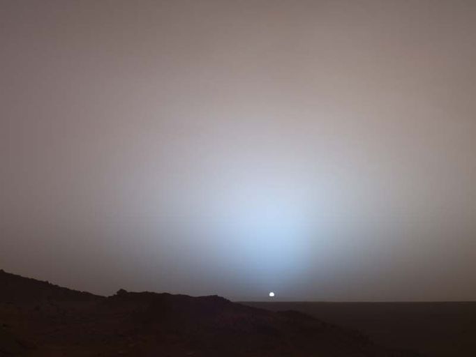 A Moment Frozen in Time 6/10/05 On May 19th, 2005, NASA's Mars Exploration Rover Spirit captured this stunning view as the Sun sank below the rim of Gusev crater on Mars. This Panoramic Camera (Pancam) mosaic was taken around 6:07 in the evening of the rover's 489th martian day, or sol. Spirit was commanded to stay awake briefly after sending that sol's data to the Mars Odyssey orbiter just before sunset. This small panorama of the western sky was obtained using Pancam's 750-nanometer, 530-nanometer and 430-nanometer color filters. This filter combination allows false color images to be generated that are similar to what a human would see, but with the colors slightly exaggerated. In this image, the bluish glow in the sky above the Sun would be visible to us if we were there, but an artifact of the Pancam's infrared imaging capabilities is that with this filter combination the redness of the sky farther from the sunset is exaggerated compared to the daytime colors of the martian sky. Because Mars is farther from the Sun than the Earth is, the Sun appears only about two-thirds the size that it appears in a sunset seen from the Earth. The terrain in the foreground is the rock outcrop "Jibsheet", a feature that Spirit has been investigating for several weeks (rover tracks are dimly visible leading up to Jibsheet). The floor of Gusev crater is visible in the distance, and the Sun is setting behind the wall of Gusev some 80 km (50 miles) in the distance. This mosaic is yet another example from MER of a beautiful, sublime martian scene that also captures some important scientific information. Specifically, sunset and twilight images are occasionally acquired by the science team to determine how high into the atmosphere the martian dust extends, and to look for dust or ice clouds. Other images have shown that the twilight glow remains visible, but increasingly fainter, for up to two hours before sunrise or after sunset. The long martian twilight (compared to Earth's) is caused by sunlight scattered around to the night side of the planet by abundant high altitude dust. Similar long twilights or extra-colorful sunrises and sunsets sometimes occur on Earth when tiny dust grains that are erupted from powerful volcanoes scatter light high in the atmosphere. Image Credit: NASA/JPL/Texas A /Cornell