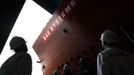 Workers watch as the forward section of the aircraft carrier HMS Queen Elizabeth is moved onto a barge at HM Naval Base in Portsmouth, southern England May 14, 2012. The hull will be transported by a sea going barge to Rosyth in Scotland where the ship will be assembled in dry dock. REUTERS/Luke MacGregor (BRITAIN - Tags: BUSINESS EMPLOYMENT MILITARY) Published: Kvě. 14, 2012, 2:22 odp.