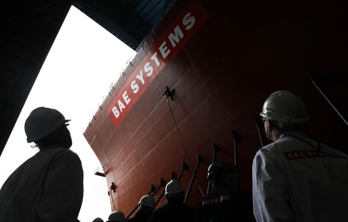 Workers watch as the forward section of the aircraft carrier HMS Queen Elizabeth is moved onto a barge at HM Naval Base in Portsmouth, southern England May 14, 2012. The hull will be transported by a sea going barge to Rosyth in Scotland where the ship will be assembled in dry dock. REUTERS/Luke MacGregor (BRITAIN - Tags: BUSINESS EMPLOYMENT MILITARY) Published: Kvě. 14, 2012, 2:22 odp.