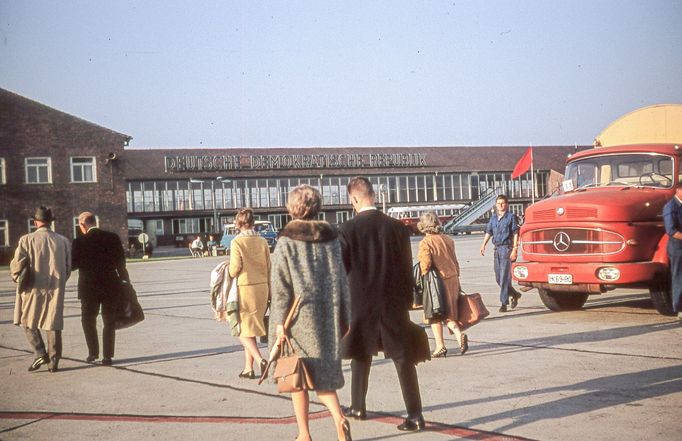 Cestující před budovou letiště Schönefeld v Berlíně, 1963. V popředí červený autobus Mercedes, na budově nápis "Deutsche Demokratische Republik".