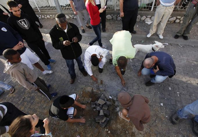 Israelis survey the damage to a road after a rocket fired from Gaza landed in the southern city of Ashdod November 16, 2012. Israel has started drafting 16,000 reserve troops, the military said on Friday, in a sign that violence could escalate further with Palestinian militants in the Gaza Strip. REUTERS/Amir Cohen (ISRAEL - Tags: POLITICS CIVIL UNREST MILITARY) Published: Lis. 16, 2012, 7:42 dop.