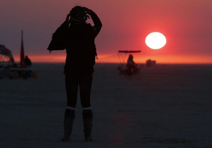 Libriel Padilla watches the sunrise as it is obscured by smoke from the western wildfire during the Burning Man 2012 "Fertility 2.0" arts and music festival in the Black Rock Desert of Nevada, August 29, 2012. More than 60,000 people from all over the world have gathered at the sold out festival, which is celebrating its 26th year, to spend a week in the remote desert cut off from much of the outside world to experience art, music and the unique community that develops.