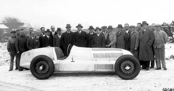 Poslední triumf velkého technika, „stříbrný šíp“ W 25: Hans Nibel (s kloboukem, první vpravo od volantu, hledící doleva).