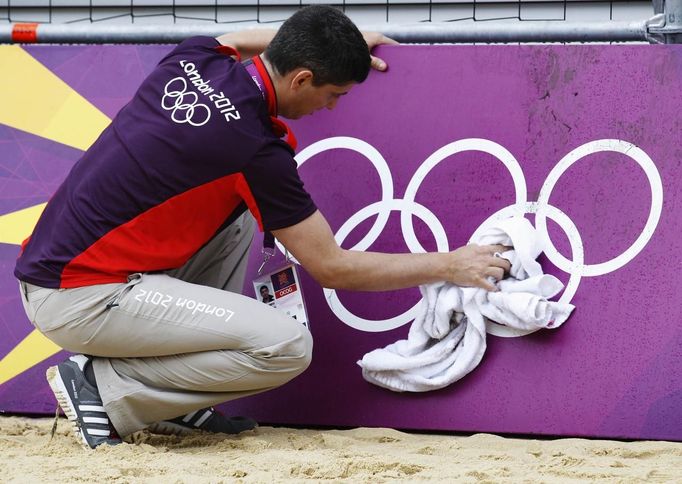 Simon Drew wipes down hoarding surrounding a practice beach volley ball court ahead of teams arriving for the London 2012 Olympic Games in London July 16, 2012. The London 2012 Olympic Games start in 11 days time. REUTERS/Luke MacGregor (BRITAIN - Tags: SPORT VOLLEYBALL OLYMPICS) Published: Čec. 16, 2012, 4:12 odp.