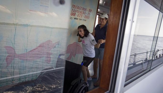 Marcilene Castro assists her daughter Alice, 17, who suffers from mild cerebral palsy, inside a boat before taking her to a "Bototherapy" session at Arau River in Amazon August 11, 2012. The "Bototherapy", a "Rolfing" therapeutic practice assisted by river dolphins, was developed by Igor Andrade, a physiotherapist, and the treatment is free for children with disabilities or disorders from low income families. Picture taken August 11, 2012. REUTERS/Bruno Kelly (BRAZIL - Tags: SOCIETY HEALTH) Published: Srp. 28, 2012, 1:59 dop.