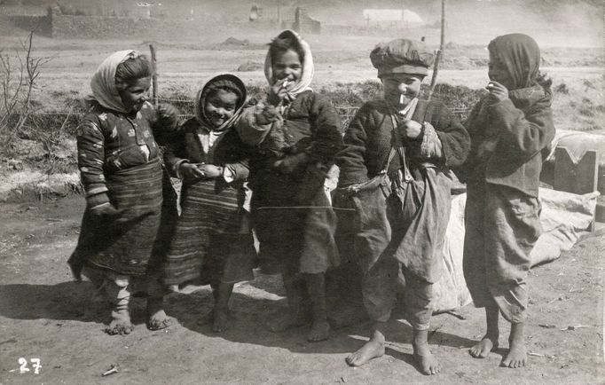 S cigaretou v ruce pózovaly německému fotografovi i romské děti stojící na tomto snímku před křesťanským hřbitovem. Datace fotografie: rok 1917.