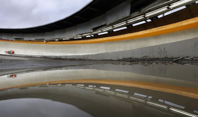 Latvia's Tomass Dukurs is seen on the track reflected in a puddle during the men's skeleton test event at the "Sanki" siding center in Rosa Khutor, a venue for the Sochi 2014 Winter Olympics near Sochi February 15, 2013. Although many complexes and venues in the Black Sea resort of Sochi mostly resemble building sites that are still under construction, there is nothing to suggest any concern over readiness. Construction will be completed by August 2013 according to organizers. The Sochi 2014 Winter Olympics opens on February 7, 2014. REUTERS/Kai Pfaffenbach (RUSSIA - Tags: BUSINESS CONSTRUCTION CITYSCAPE ENVIRONMENT SPORT OLYMPICS SKELETON TPX IMAGES OF THE DAY) Published: Úno. 15, 2013, 2:28 odp.