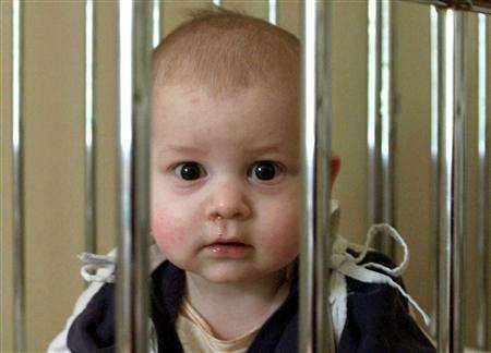 Chlapec kouká přes mříže dětské postýlky