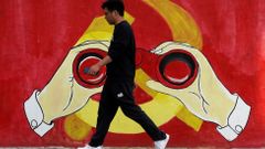 A man walks next to a mural showing an image of the Chinese Communist Party's emblem along a street in Shanghai
