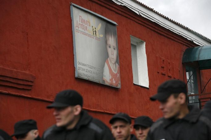 Inmates walk past a poster that reads: 'Help Children' at a high-security male prison camp outside Russia's Siberian city of Krasnoyarsk May 14, 2013. High-security male prison camp number 17 is intended to house male inmates who are serving a sentence for the first time, and have been convicted for serious crimes. Prisoners at the facility work in wood and metal processing shops, manufacture furniture, sew clothes and do other kinds of work. They can also take part in educational, sport and cultural programs. Picture taken May 14, 2013. REUTERS/Ilya Naymushin (RUSSIA - Tags: CRIME LAW SOCIETY) ATTENTION EDITORS: PICTURE 6 OF 29 FOR PACKAGE 'INSIDE SIBERIA'S PRISONS' SEARCH 'ILYA PRISON' FOR ALL IMAGES Published: Čer. 19, 2013, 10:02 dop.